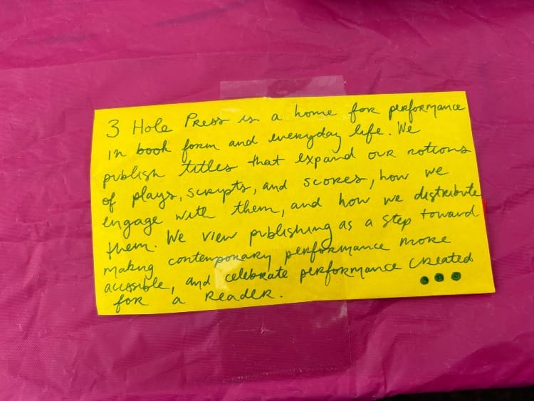 a handwritten yellow note card has the same text as above, with the mission of 3 Hole Press