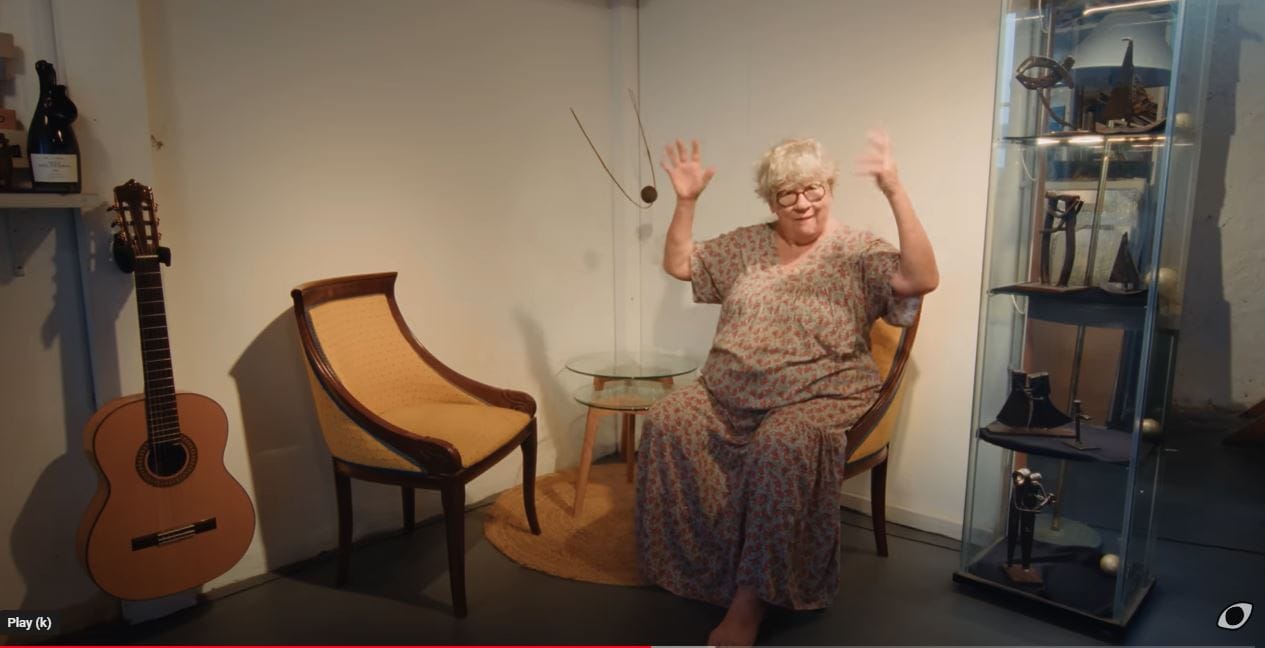 an older woman is seated in a chair with both hands raised