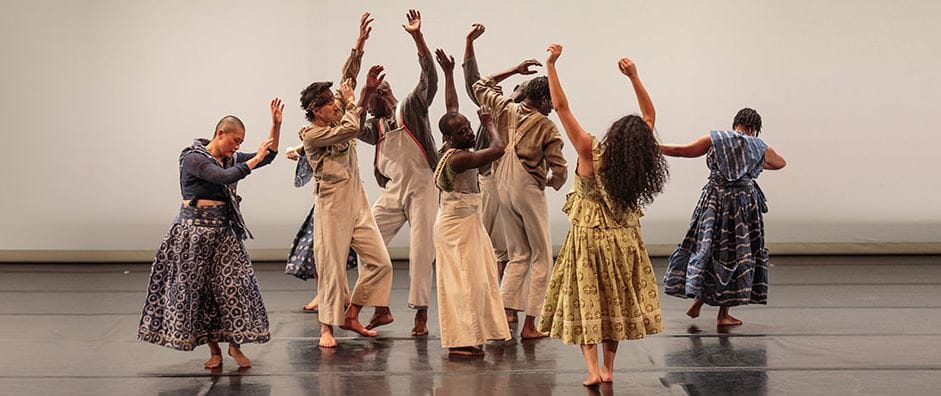 a group of nine dancers in a clump, most facing away from the camera